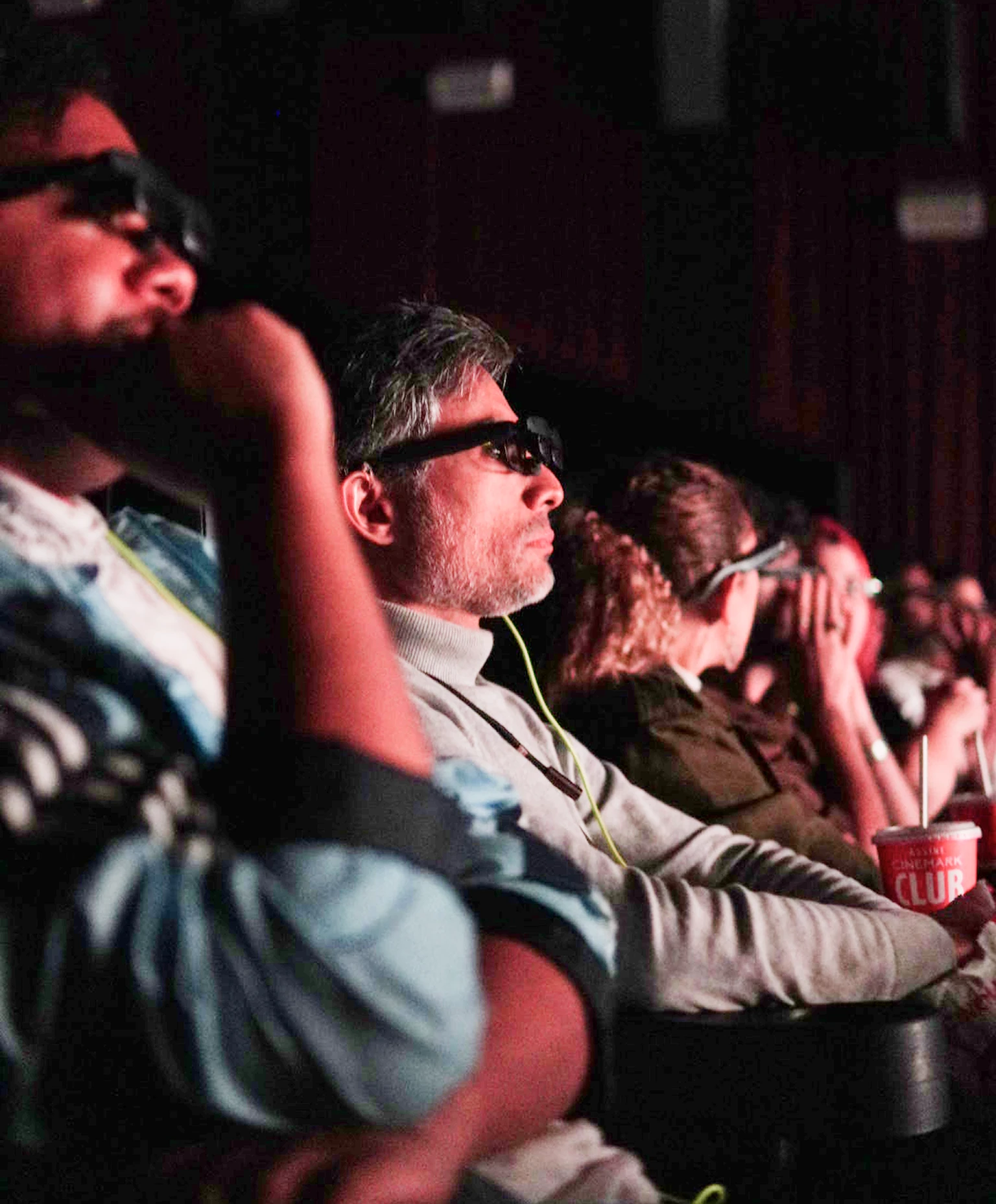 Plateia de cinema usando os óculos PingPlay durante uma sessão, iluminada pelos refletores da sala
